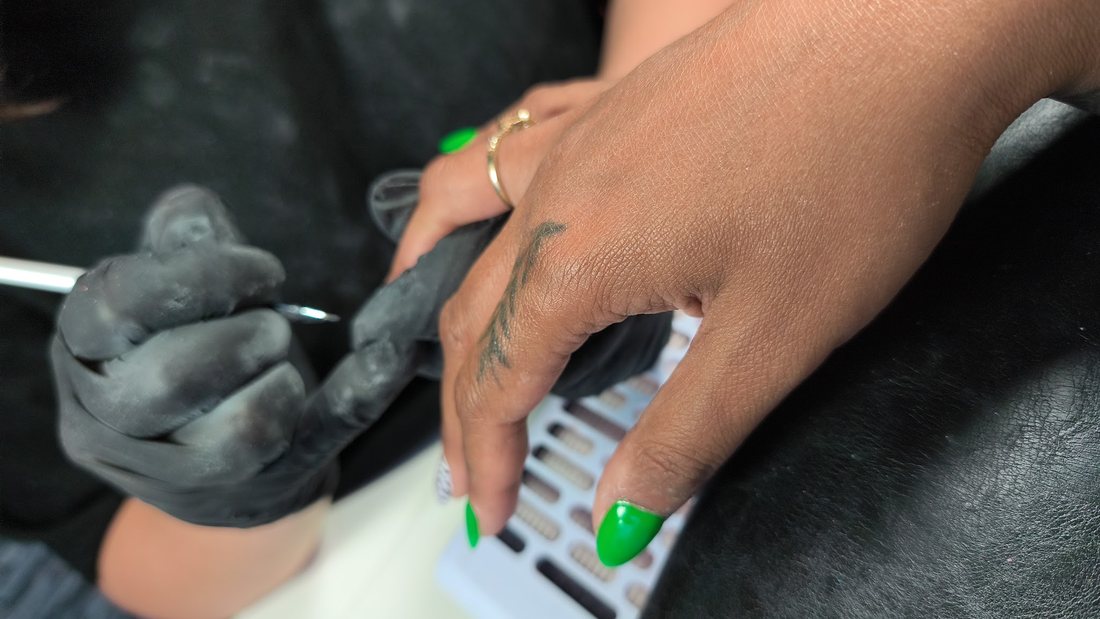 Marieke vijlt met zwarte handschoenen de groene nagels van een klant bij haar werktafel